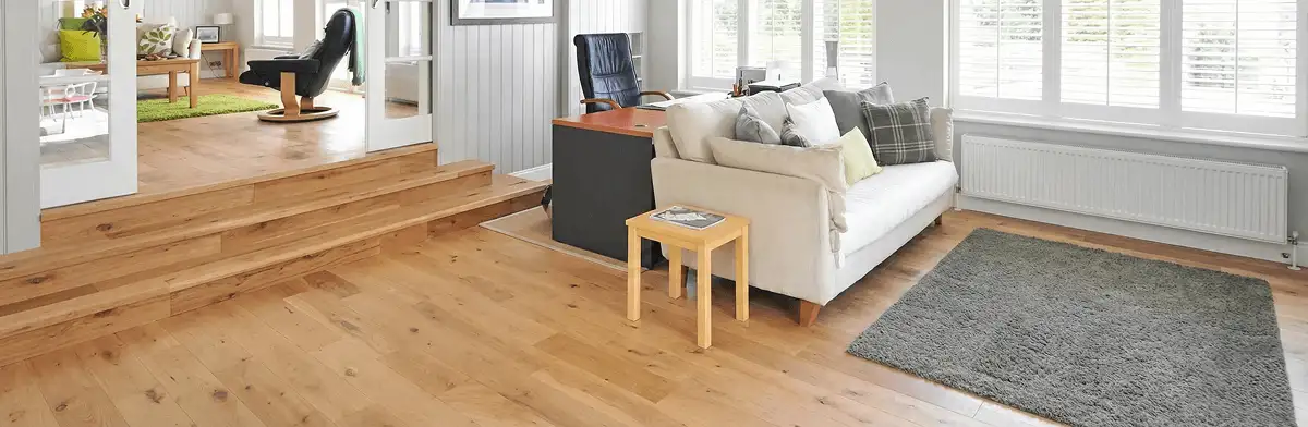 A modern living room with professionally installed laminate flooring, a beige sofa, a small side table, a gray rug, and large windows with white shutters in Austin, TX